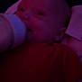 baby, bottle, feeding, infant, red_clothing, dark_background, face, head, person, closeup, indoors, child, drink, sleepwear, young, portrait, feeding_bottle, blur, low_light, candid