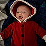 baby, blanket, buttoned_clothing, child, cozy, cute, face, happy, hood, indoor, infant, infant_clothing, lying_down, pacifier, portrait, red_onesie, smiling, soft_fabric, warm_clothing, young_child