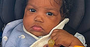 Zion joined the competition — help win amazing prizes! baby, child, car_seat, pacifier, toy, orange_toy, hair_clips, blue_blanket, clothing, face, hand, infant, seatbelt, closeup, cute, indoors, sitting, expression, person, portrait