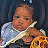 baby, child, car_seat, pacifier, toy, orange_toy, hair_clips, blue_blanket, clothing, face, hand, infant, seatbelt, closeup, cute, indoors, sitting, expression, person, portrait
