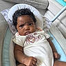 baby, infant, onesie, text_on_clothing, indoor, cushion, baby_seat, living_room, furniture, person, cute, child, closeup, portrait, skin, hair, expression, fist, comfort, home