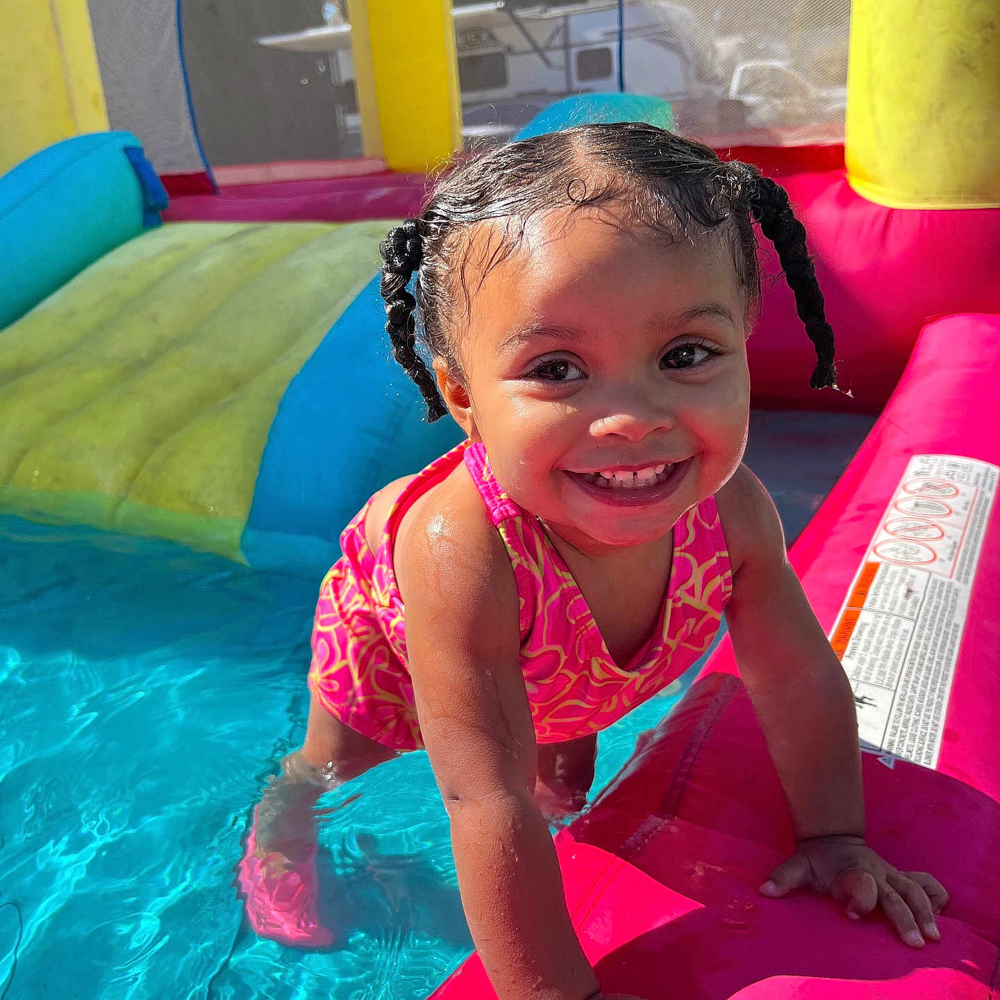 Lylah is registered to the contest to win money with this photo: braided_hair, child, colorful, cute, fun, happy, inflatable_pool, outdoor, person, play, pool, smile, splash, summer, sunlight, swimsuit, toddler, toy, water, young_child