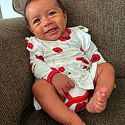 Eila is registered to the contest to win money with this photo: baby, child, clothing, couch, cute, face, feet, furniture, happy, human, indoors, infant, legs, portrait, red_flowers, seated, skin, smiling, white_dress, young_child