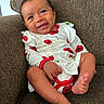 baby, child, clothing, couch, cute, face, feet, furniture, happy, human, indoors, infant, legs, portrait, red_flowers, seated, skin, smiling, white_dress, young_child