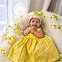 adorable, baby, bow, child, cozy, cute, flower_decor, fluffy_blanket, hands_clasped, happy, headband, indoor, infant, portrait, seated, smiling, soft_lighting, soft_texture, yellow_dress, yellow_flowers