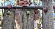 Hollie joined the competition — help win amazing prizes! blonde_hair, child, climbing, daylight, face, forest, happy, jacket, outdoor, park, photography, pink_clothing, play_structure, playground, portrait, smiling, sunny, toddler, trees, wooden_bars