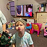 Hollie is registered to the contest to win money with this photo: child, toddler, portrait, indoor, playroom, hat, leopard_print, pouting, duck_face, smiling, face, person, toys, toy_cart, television, cartoon, furniture, home, colorful, family