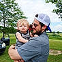 Asher is registered to the contest to win money with this photo: man, baby, child, outdoor, grass, tree, car, cap, sunglasses, holding, expression, sky, cloud, park, casual_clothing, greenery, daytime, person, nature, family