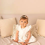 Avaluna participe au concours pour gagner de l'argent avec cette photo : toddler, child, girl, white_dress, headband, barefoot, bed, pillow, beige, cozy, portrait, indoor, cute, smiling, young_child, sitting, soft_lighting, photography, neutral_colors, watermark