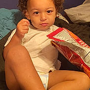 Landan joined the competition — help win amazing prizes! bed, blanket, candid, casual, child, chips, comfortable, curly_hair, diaper, expression, food, indoor, person, pillow, portrait, relaxed, snack, toddler, white_shirt, young_child