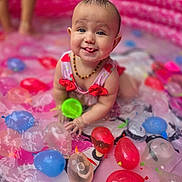 Abriella is registered to the contest to win money with this photo: baby, blue, child, colorful, cute, fun, happy, inflatable_pool, necklace, outdoor, pink, playful, red, sleeveless, smiling, splash, summer, tongue_out, water, water_balloons