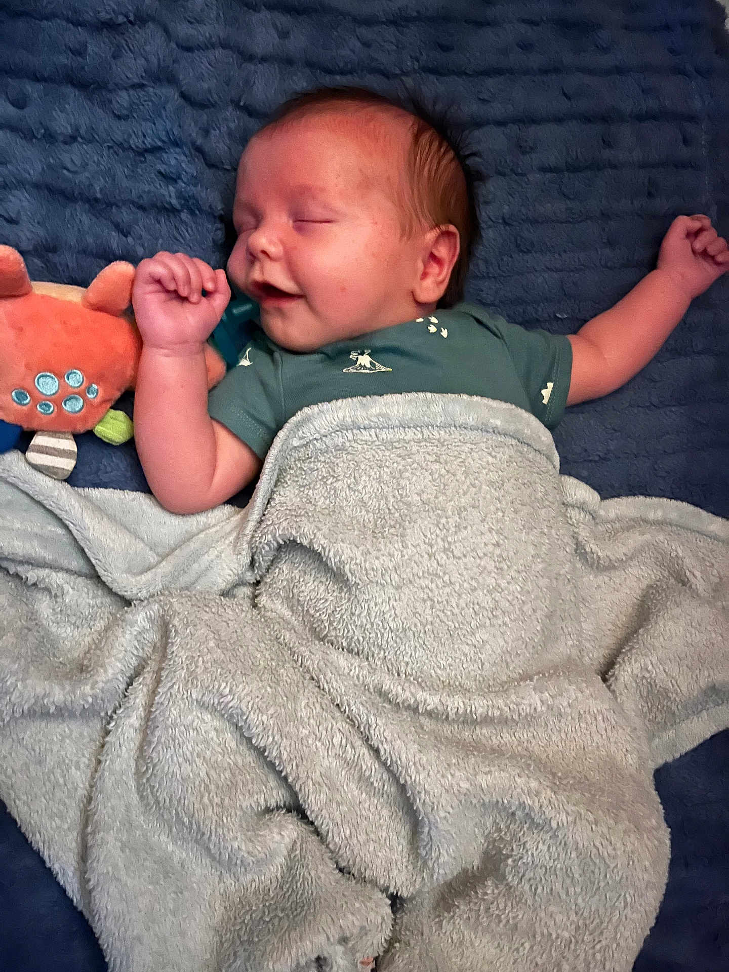 Michael is registered to the contest to win money with this photo: baby, sleeping, blanket, plush_toy, blue_blanket, cozy, infant, peaceful, smiling, child, soft_texture, cute, resting, toddler, clothing, nap, indoor, relaxing, happy, portrait