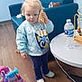 toddler, child, toy_phone, blue_sweater, indoor, wooden_floor, blue_couch, white_table, water_bottle, bead_maze, ride_on_toy, pink_toy_car, shoes, playing, pretending, young_child, person, floor, furniture, casual_clothing