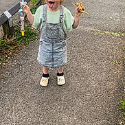Lilly-Sue joined the competition — help win amazing prizes! child, playful, tongue_out, denim_dress, pastel_cap, toy_dinosaur, pacifier_clip, outdoor, paved_path, fence, greenery, cute, smiling, casual_clothing, footwear, socks, person, happy, nature, daytime