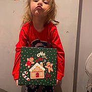 Lilly-Sue joined the competition — help win amazing prizes! child, cute, decorations, expression, face, fan, floor, gingerbread_box, hair, holding, holiday_theme, home, indoor, pajamas, poster, pout, red_shirt, standing, toy_box, wall