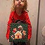child, cute, decorations, expression, face, fan, floor, gingerbread_box, hair, holding, holiday_theme, home, indoor, pajamas, poster, pout, red_shirt, standing, toy_box, wall