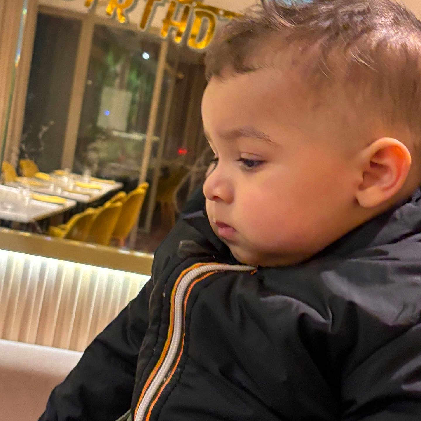 Jad a rejoint le concours — aidez-le/la à gagner de superbes lots ! baby, birthday_banner, celebration, chairs, cheeks, child, close_up, coat, dining_table, festive, hair, indoor, jacket, party, pensive, person, portrait, profile, restaurant, toddler