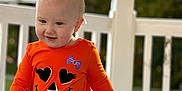 Allison is registered to the contest to win money with this photo: bow, casual_clothing, child, cute, daylight, expression, fall, happy, headwear, nature, orange_clothing, outdoor, person, playful, porch, railing, smile, toddler, walking, young_child