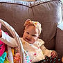 baby, smiling, headband, sweater, polka_dot, couch, basket, toys, colorful, indoor, child, happy, cute, infant, playful, fabric, pattern, relaxing, home, portrait