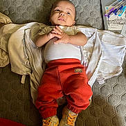 Ezair is registered to the contest to win money with this photo: baby, baby_clothes, blanket, carpet, casual, child, clothing, curious_expression, floor, footwear, hand_gesture, indoor, infant, lying_down, orange_pants, pens, person, sketchbook, sneakers, white_onesie