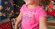 Delilah joined the competition — help win amazing prizes! child, smiling, portrait, indoor, christmas, christmas_tree, holiday, gift_boxes, gift_bags, stockings, pink_shirt, jeans, curly_hair, standing, home, living_room, festive, celebration, carpet, football_chair