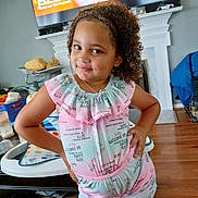 Delilah joined the competition — help win amazing prizes! child, girl, portrait, smiling, curly_hair, standing, hands_on_hips, colorful_clothing, dress, shorts, necklace, indoors, living_room, television, fireplace, wood_floor, high_chair, furniture, home, photography