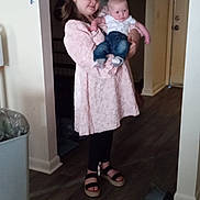 Susie is registered to the contest to win money with this photo: child, baby, girl, infant, sibling, holding, portrait, indoors, hallway, home, pink_dress, white_shirt, blue_jeans, sandals, smiling, standing, family, doorway, hardwood_floor, laundry_basket
