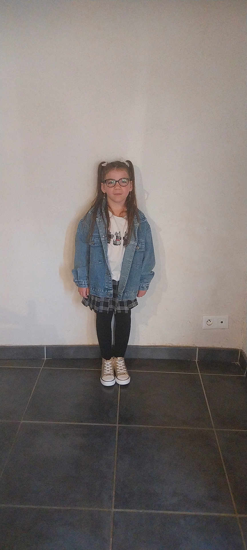 Hilona a rejoint le concours — aidez-le/la à gagner de superbes lots ! child, girl, glasses, denim_jacket, plaid_skirt, black_tights, sneakers, standing, indoor, plain_wall, tile_floor, casual_clothing, long_hair, pigtails, earrings, young, portrait, full_body, smile, fashion