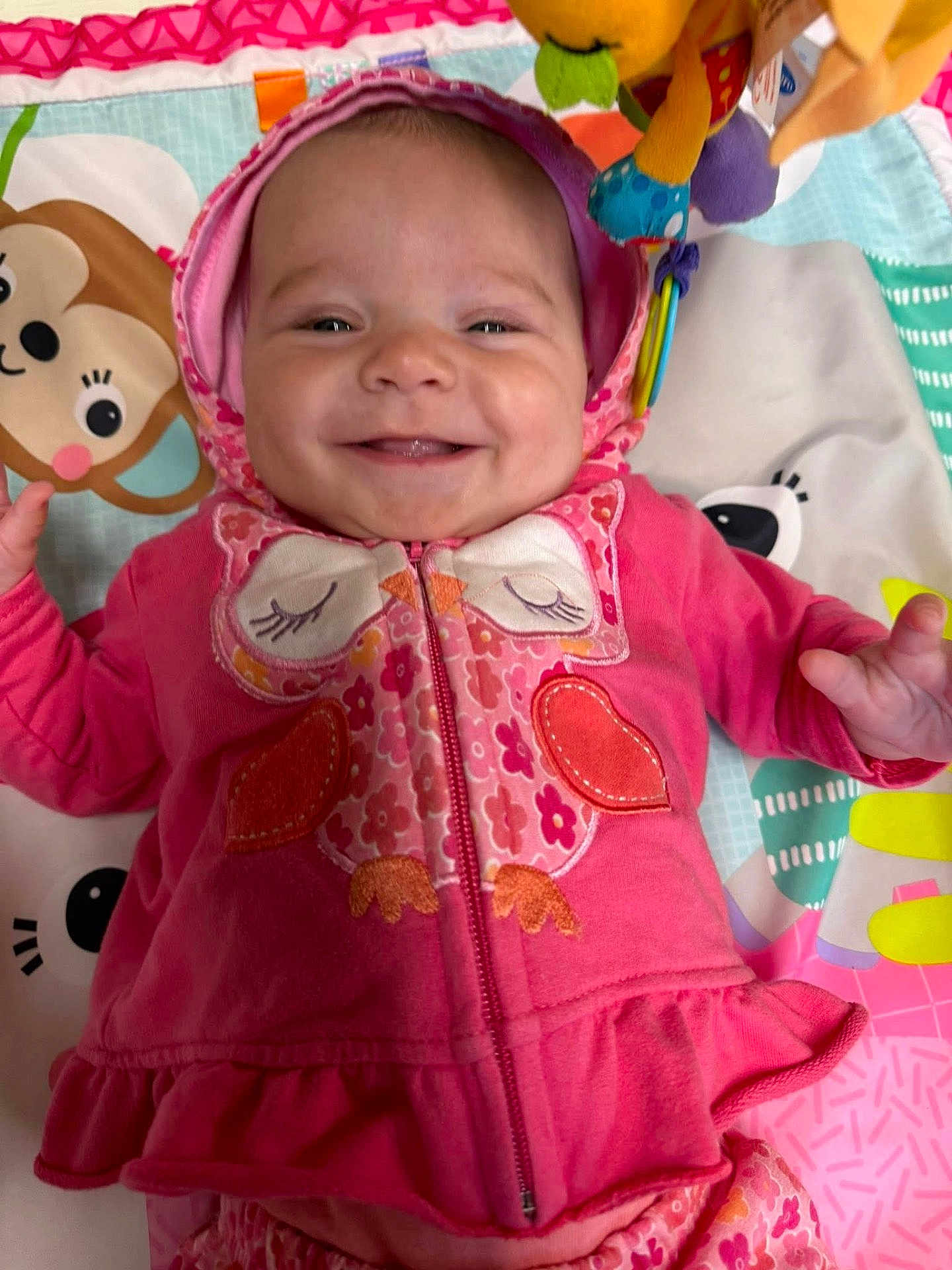 Marti joined the competition — help win amazing prizes! baby, smiling, hoodie, pink_clothing, owl_design, play_mat, toy, infant, happy, child, cute, indoors, colorful, lying_down, face, young_child, apparel, patterned_clothing, cheerful, closeup