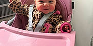 Marti joined the competition — help win amazing prizes! baby, high_chair, pink, smiling, indoor, child, leopard_print, clothing, seat_belt, window, wall, cheerful, cute, infant, person, happy, waving, furniture, face, head