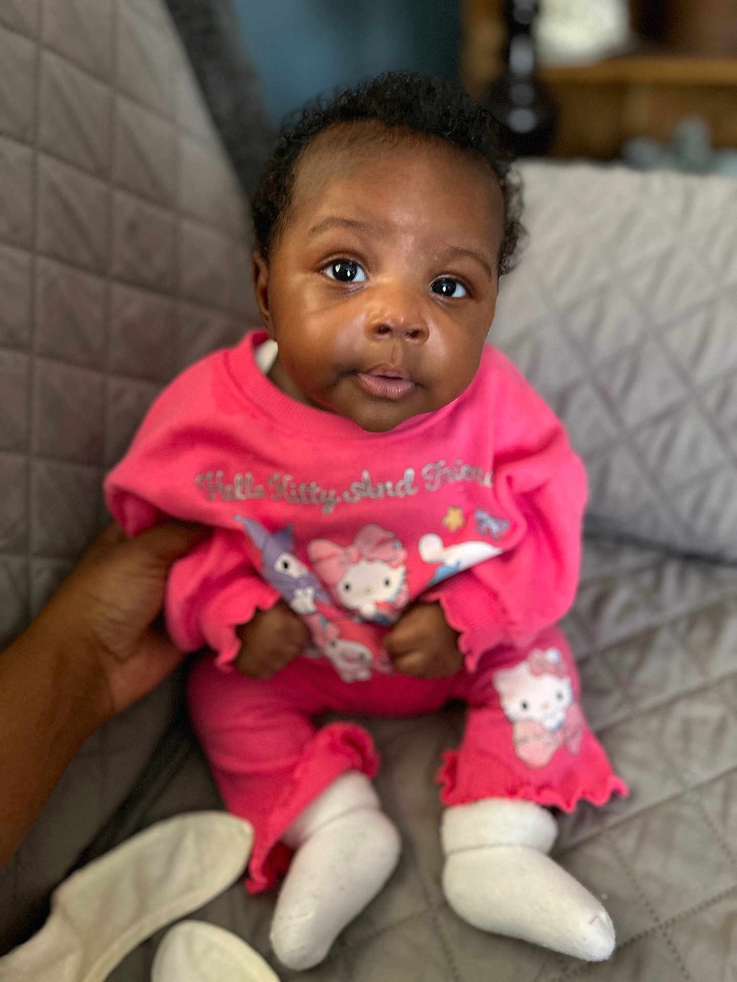 Sai is registered to the contest to win money with this photo: baby, child, infant, pink_clothing, hello_kitty, pajamas, socks, quilted_blanket, hand, indoor, person, cute, face, eyes, seated, cozy, soft_lighting, portrait, comfort, curious