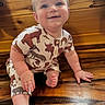 baby, child, smiling, sitting, wooden_floor, animal_print_clothing, onesie, cute, happy, indoor, portrait, infant, small_hands, small_feet, blue_eyes, light_hair, wood_paneling, candid, closeup, adorable