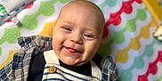 Lalo a rejoint le concours — aidez-le/la à gagner de superbes lots ! baby, smiling, child, striped_overalls, plaid_shirt, colorful_mat, patterned_mat, happy, tongue_out, cute, infant, clothing, portrait, lying_down, indoors, cheerful, face, person, playmat, closeup