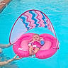 Olivia joined the competition — help win amazing prizes! baby, infant, child, pool, swimming_pool, float, inflatable, pink, water, outdoor, swimwear, canopy, adult_hands, recreation, summer, portrait, sitting, relaxed, poolside, water_safety