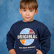 Rayan participe au concours pour gagner de l'argent avec cette photo : child, boy, portrait, blue_background, sweatshirt, casual_clothing, smile, standing, hands_on_hips, short_hair, indoor, studio, confident, cute, young, fashion, childhood, person, apparel, expression