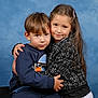 child, children, boy, girl, hug, portrait, studio, blue_background, sweatshirt, jacket, long_hair, hair_clip, smile, candid, tender_moment, sibling, affection, indoor, cute, young