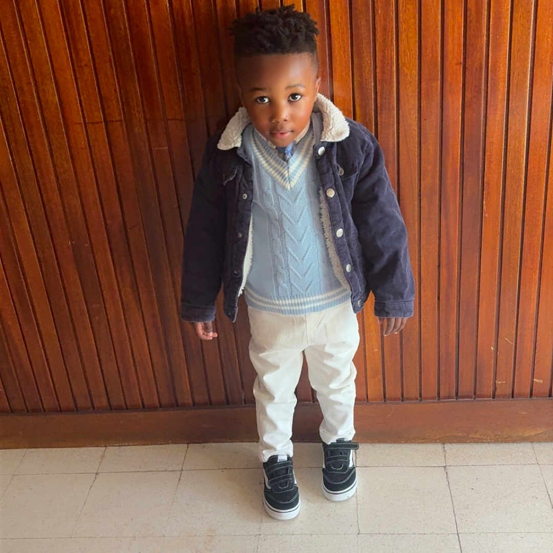 Lyel-Wilhem a rejoint le concours — aidez-le/la à gagner de superbes lots ! black_hair, boy, casual, child, curious, fashion, floor, indoor, jacket, looking_up, pants, person, portrait, sneakers, standing, sweater, tile_floor, warm_colors, wooden_wall, young