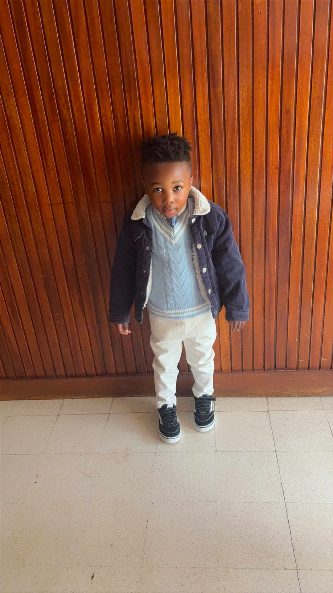 Lyel-Wilhem a rejoint le concours — aidez-le/la à gagner de superbes lots ! black_hair, boy, casual, child, curious, fashion, floor, indoor, jacket, looking_up, pants, person, portrait, sneakers, standing, sweater, tile_floor, warm_colors, wooden_wall, young