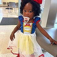 Emmy joined the competition — help win amazing prizes! child, toddler, costume, snow_white, red_bow, pacifier, curly_hair, dress, yellow_skirt, blue_top, indoor, chair, floor, waiting_room, person, shoes, table, face, expression