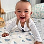 baby, smiling, crawling, bed, drool, white_clothing, patterned_sheet, indoor, child, happy, infant, cute, face, hands, furniture, home, portrait, person, young_child, baby_boy