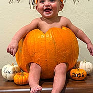 Lucius is registered to the contest to win money with this photo: autumn, baby, bare_arms, bare_feet, child, decorations, family_photo, festive, giant_pumpkin, halloween, happy, indoor, orange_hat, portrait, pumpkin, seasonal, smiling, still_life, wall, wooden_surface