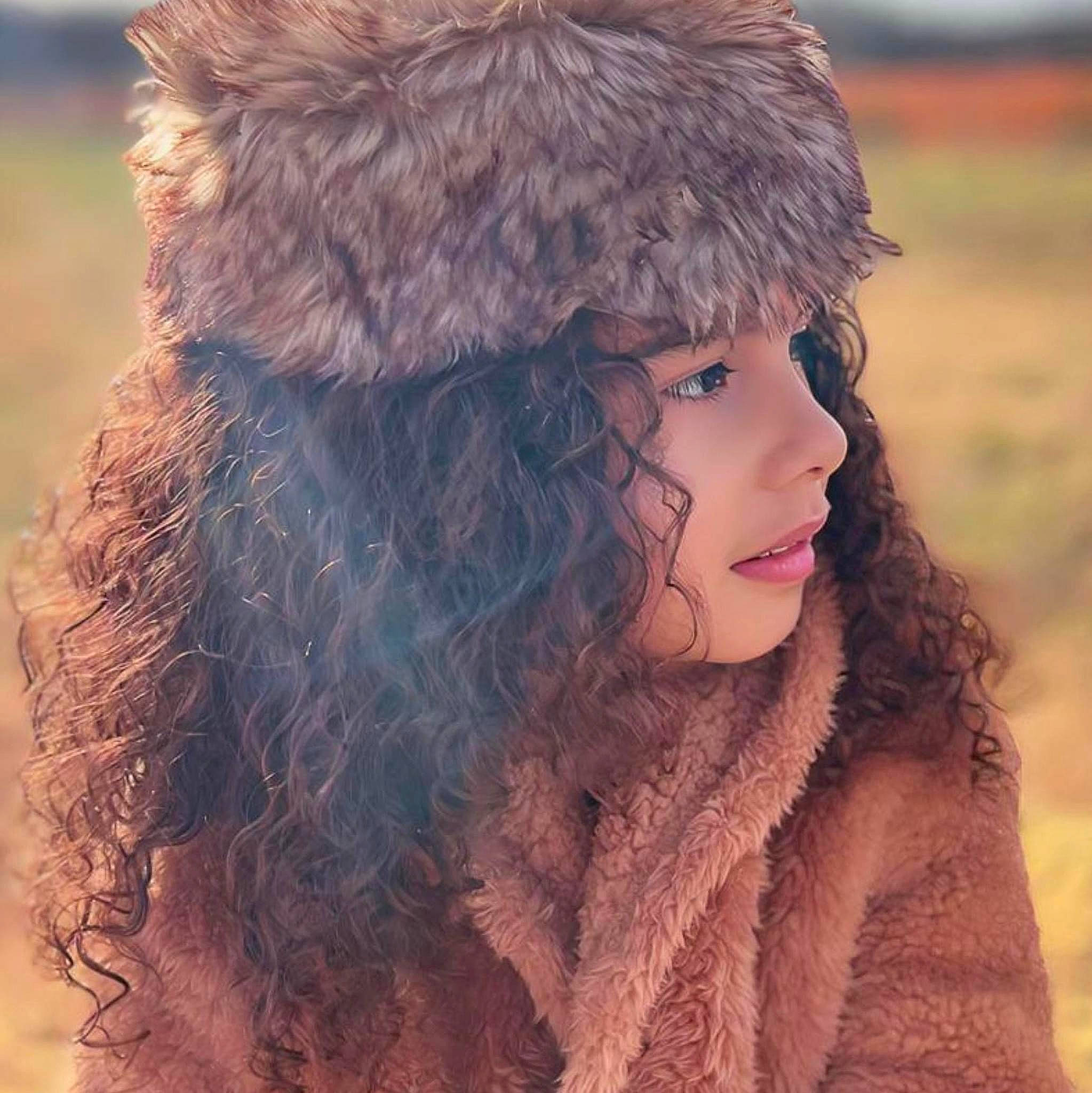 Melissa is registered to the contest to win money with this photo: animal_product, beanie, brown_hair, cap, fashion_accessory, fashion_design, feather, fur, fur_clothing, grass, happy, hat, headwear, jacket, knit_cap, long_hair, natural_material, outerwear, parka, person