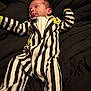baby, infant, onesie, striped_clothing, black_and_white, green_accent, tongue_out, lying_down, bed, blanket, cute, child, young, person, sleepwear, soft_fabric, indoor, portrait, expression, face