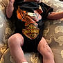 Jameson is registered to the contest to win money with this photo: baby, infant, onesie, harley_davidson, clothing, cushion, elephant_pattern, socks, legs, arms, face, portrait, indoor, person, cute, newborn, babywearing, soft_furniture, expression, relaxing