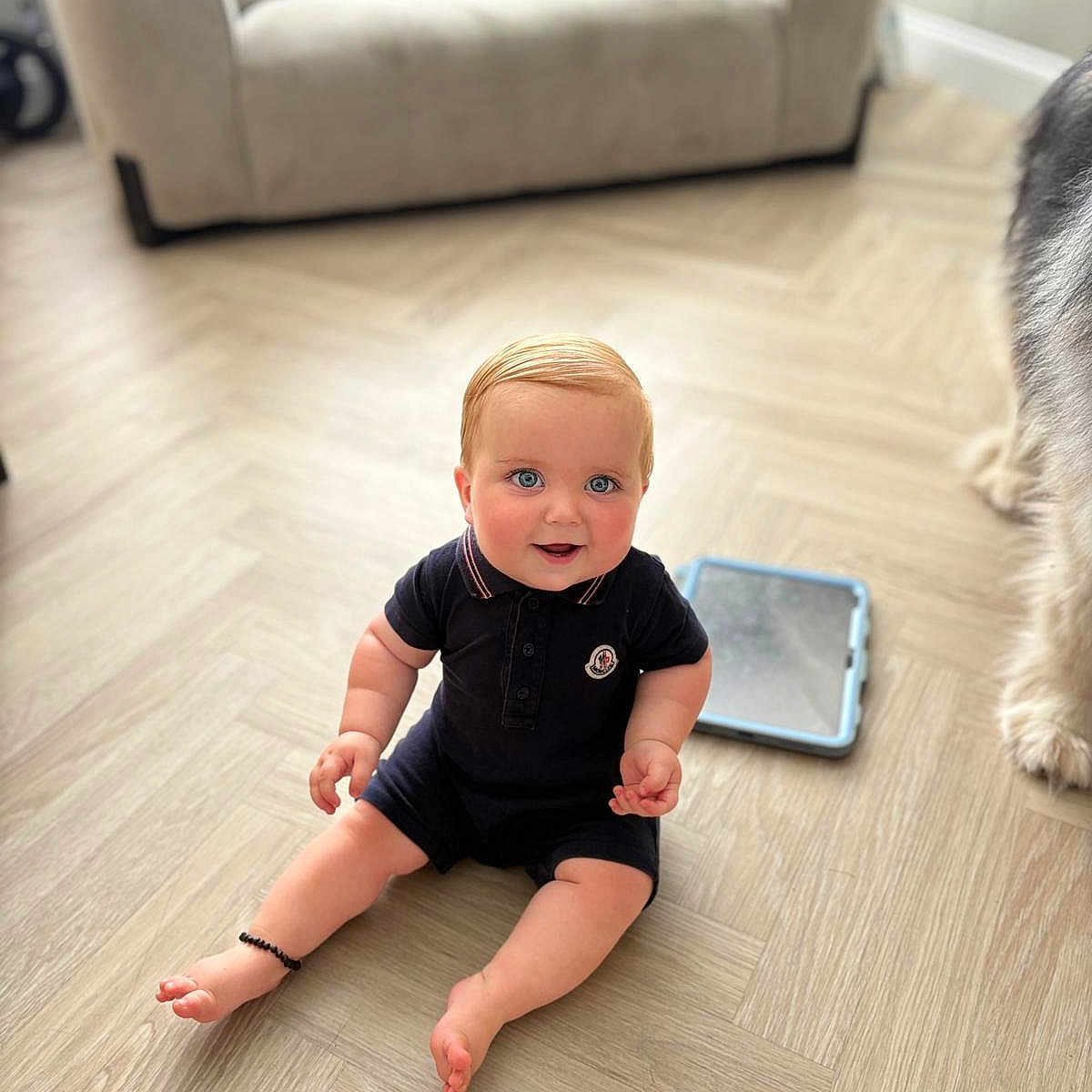 Cass is registered to the contest to win money with this photo: ankle_bracelet, baby, blue_eyes, child, couch, curious, cute, dog_paw, floor, flooring, furniture, home, indoor, pet, pillow, romper, sitting, smiling, tablet, wooden_floor