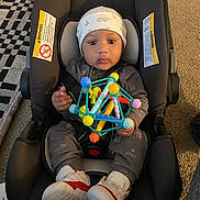 Devonte is registered to the contest to win money with this photo: baby, car_seat, toy, hat, shoes, clothing, floor, carpet, indoor, child, infant, person, footwear, geometric_toy, pattern, headwear, cute, seated, looking_at_camera, home