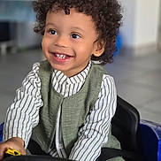 Izayah participe au concours pour gagner de l'argent avec cette photo : child, toddler, smiling, curly_hair, toy_car, steering_wheel, indoor, happy, clothing, striped_shirt, vest, person, play, cute, seatbelt, floor_tiles, portrait, young, joyful, kid
