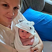 Colton is registered to the contest to win money with this photo: woman, baby, towel, hooded_towel, bear_hood, couch, blue_pillow, smile, face, indoor, person, skin, arm, hand, blanket, comfort, parent, child, cute, cozy