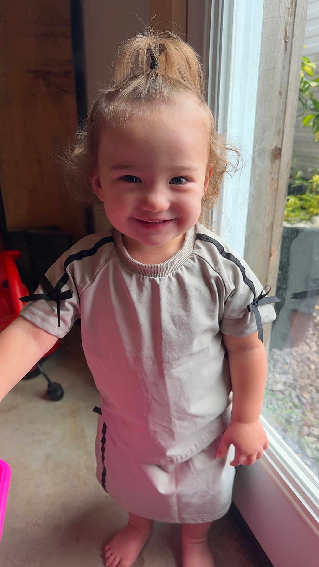 Skai joined the competition — help win amazing prizes! toddler, child, smiling, standing, barefoot, pony_tail, short_sleeves, light_clothing, ribbons, indoor, window, glass_door, concrete_floor, happy, cute, person, young_child, casual, natural_light, home