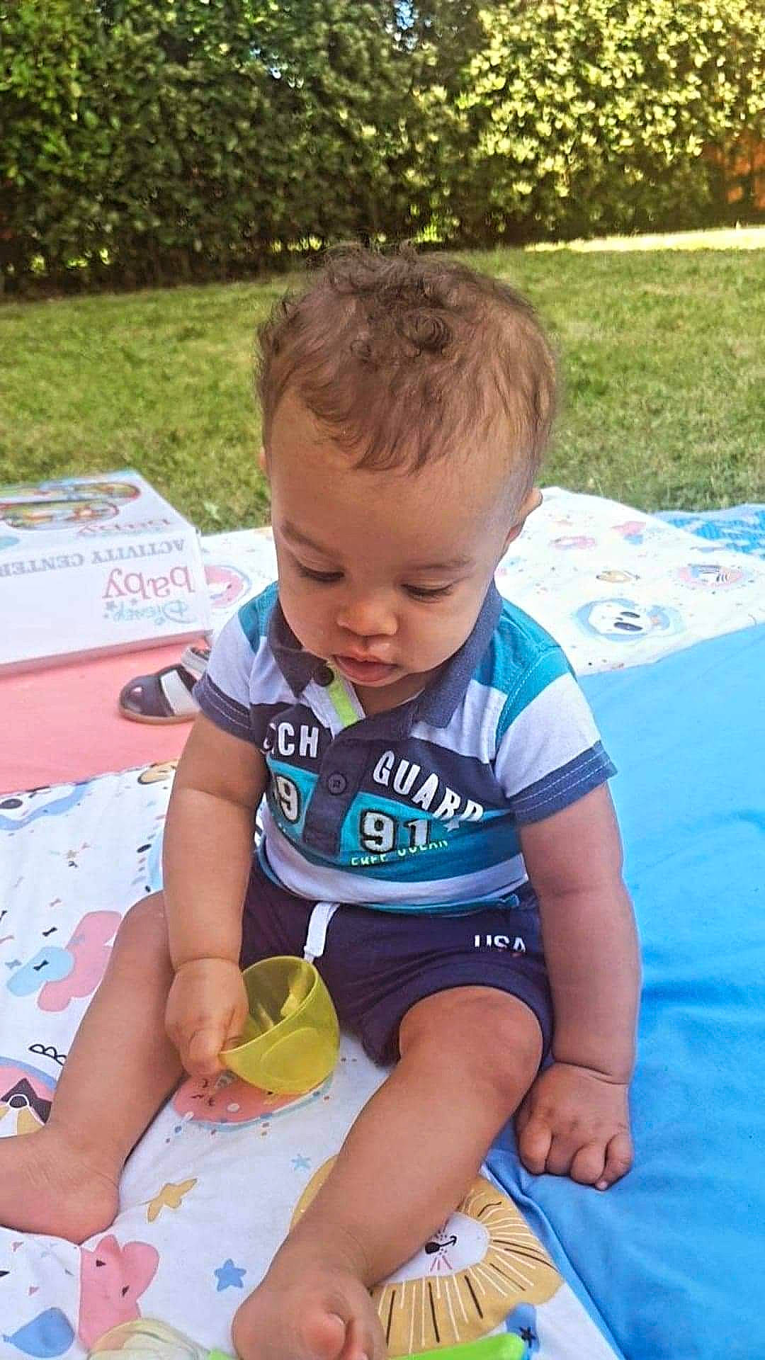 Ryan participe au concours pour gagner de l'argent avec cette photo : baby, baby_products, baby_toddler_clothing, child, fun, grass, happy, leisure, pattern, person, plant, play, recreation, shorts, sitting, sleeve, t_shirt, thigh, toddler, vacation